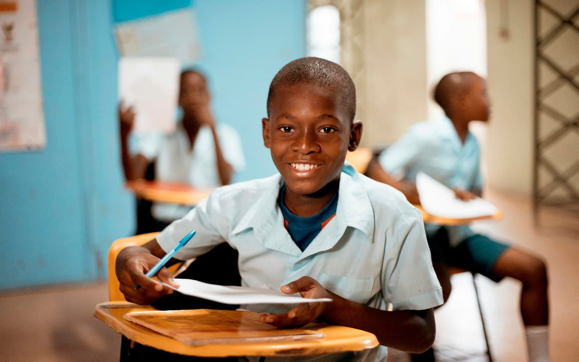 A smiling Kenyan schoolboy studying at his desk